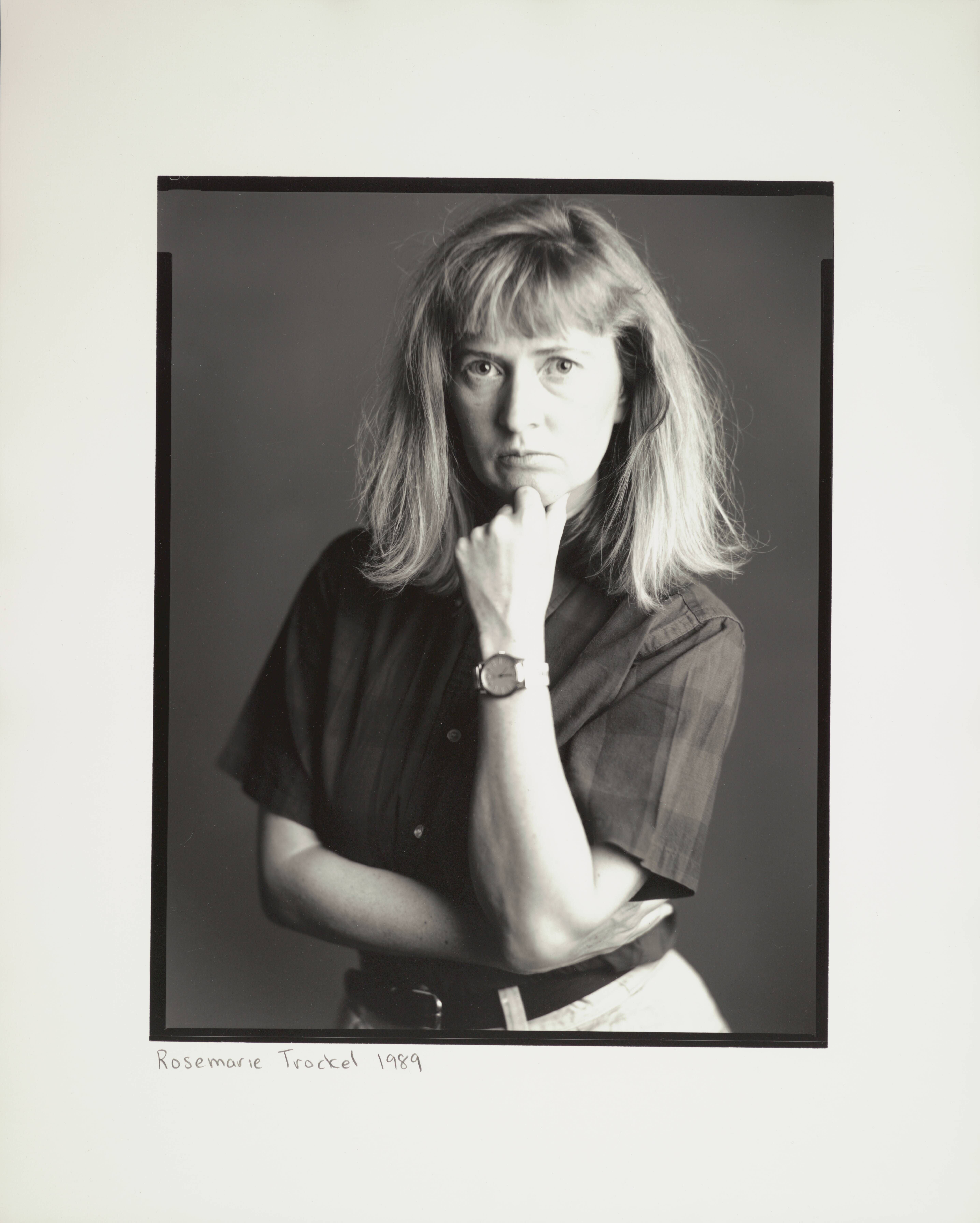 Black and white photograph shows a person with blonde hair, resting their chin on their hand. The predominant colors are shades of grey and white.