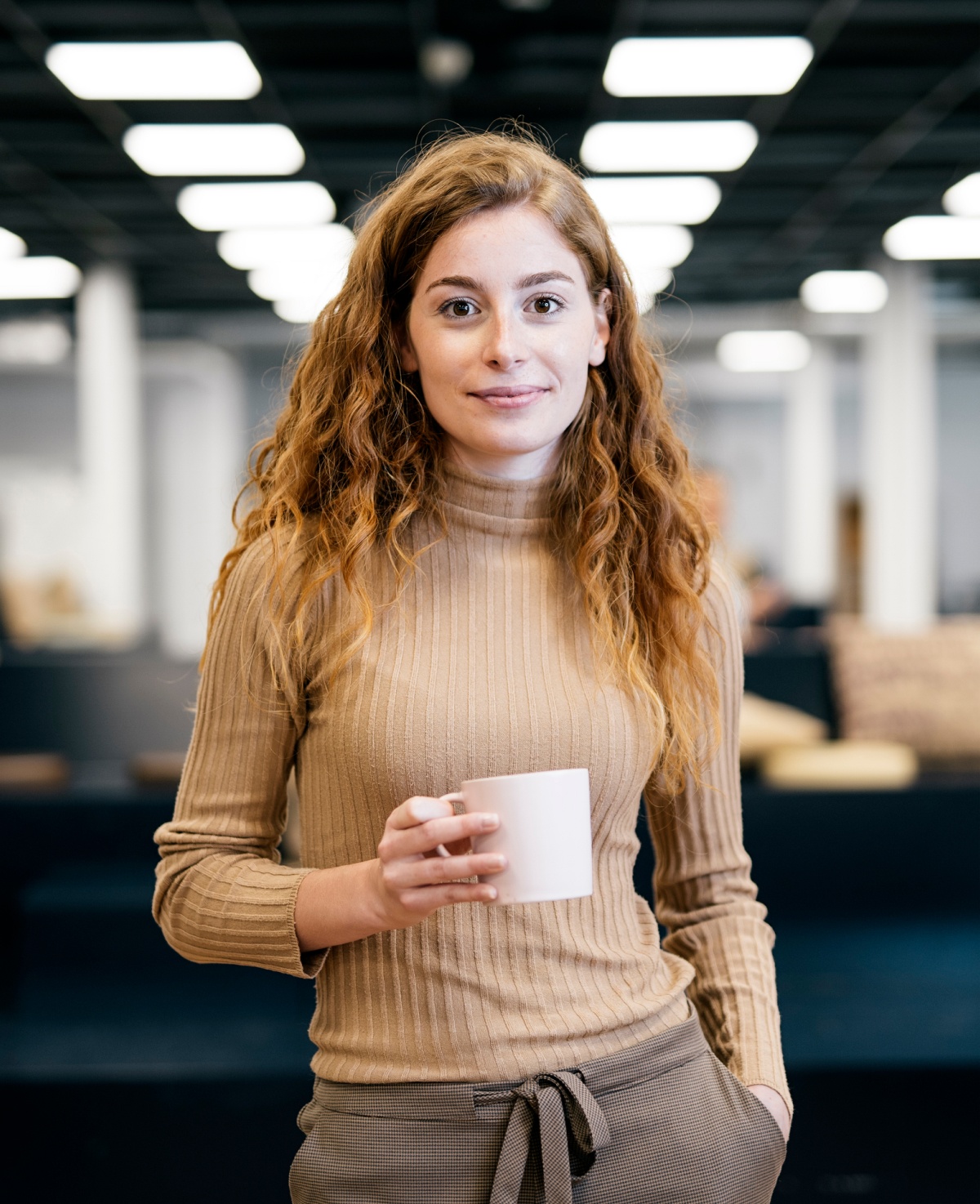 Woman standing in office drinking coffee. 