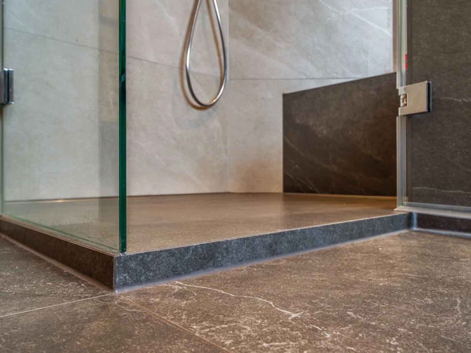 Moderne Dusche mit Glaswand und dunklem Bodenbelag.