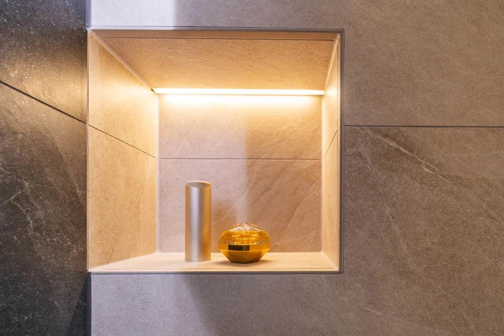 Ein beleuchteter Wandnischenbereich mit einem silbernen Behälter und einem goldenen Objekt.