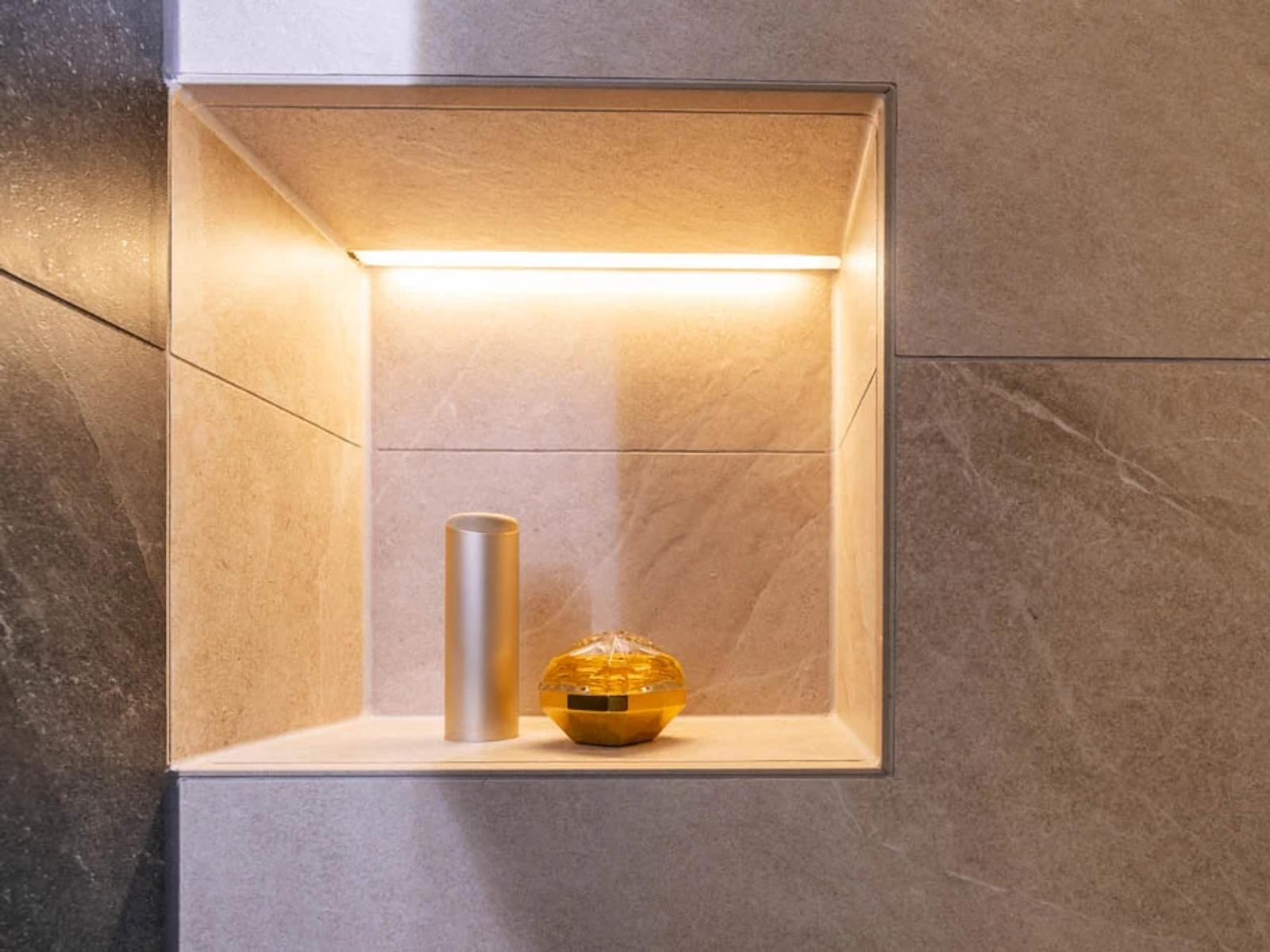 Ein beleuchteter Wandnischenbereich mit einem silbernen Behälter und einem goldenen Objekt.