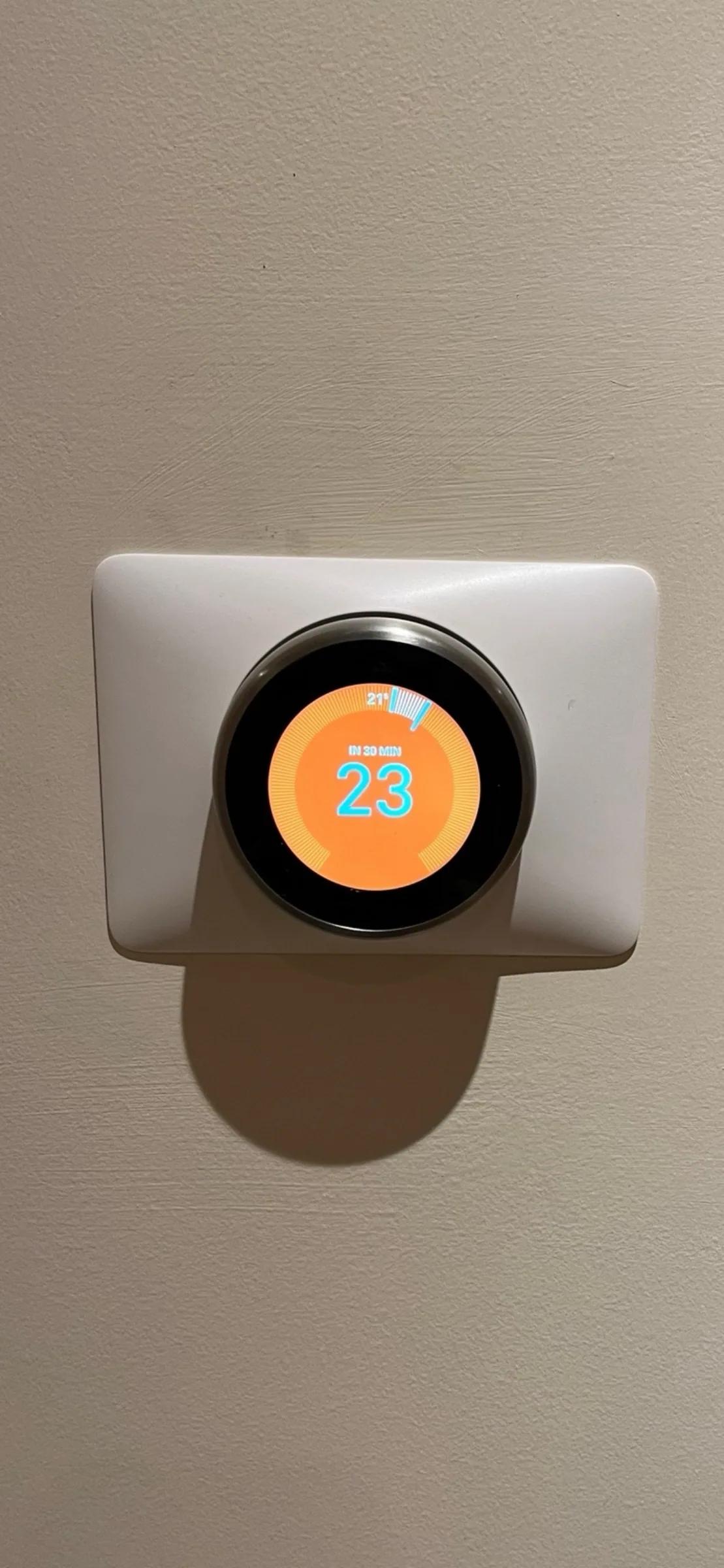 A wall-mounted smart heating control showing the room set to 23 degrees