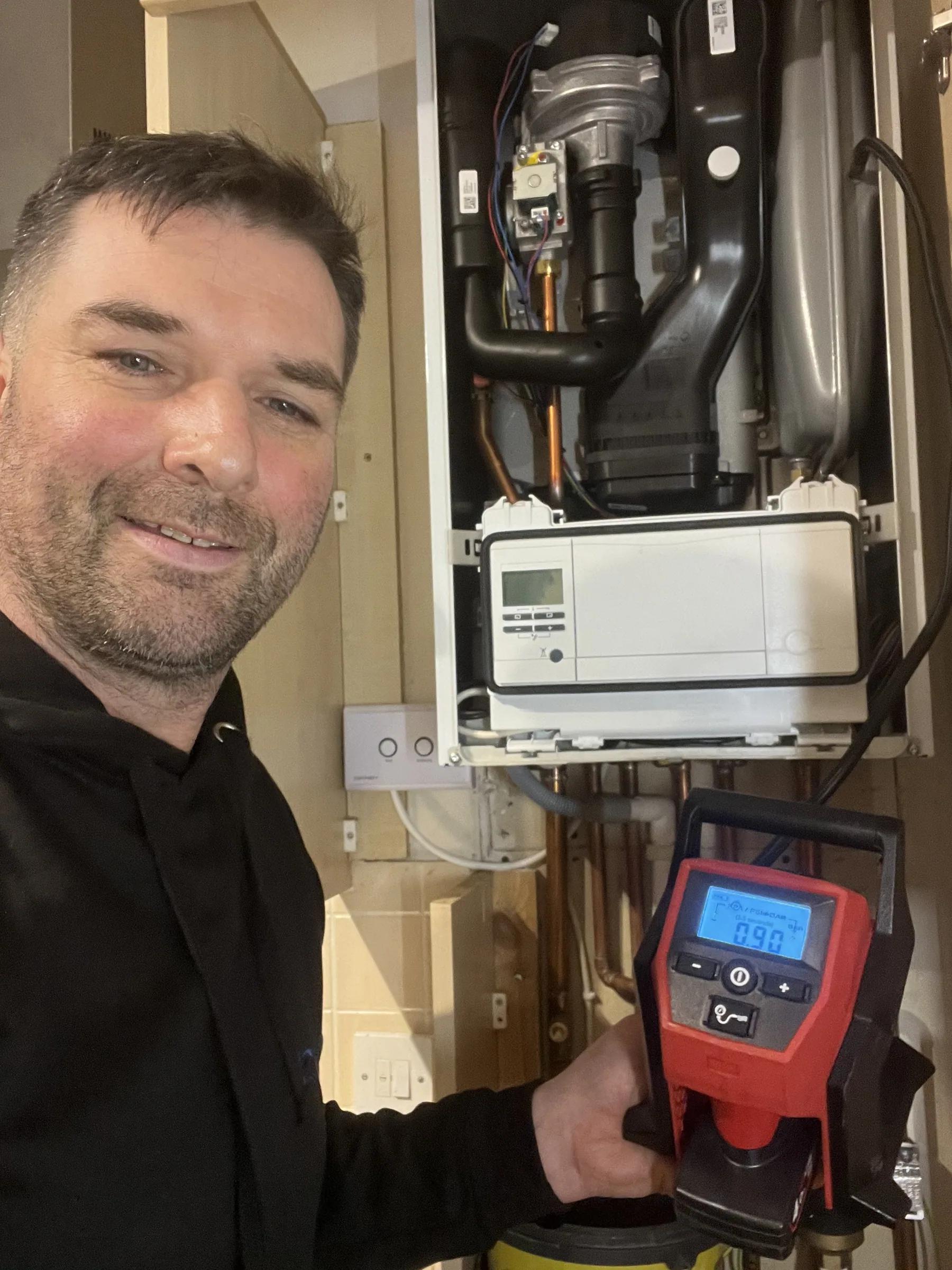 A flue gas analyser held against a boiler, showing a live combustion reading during a service