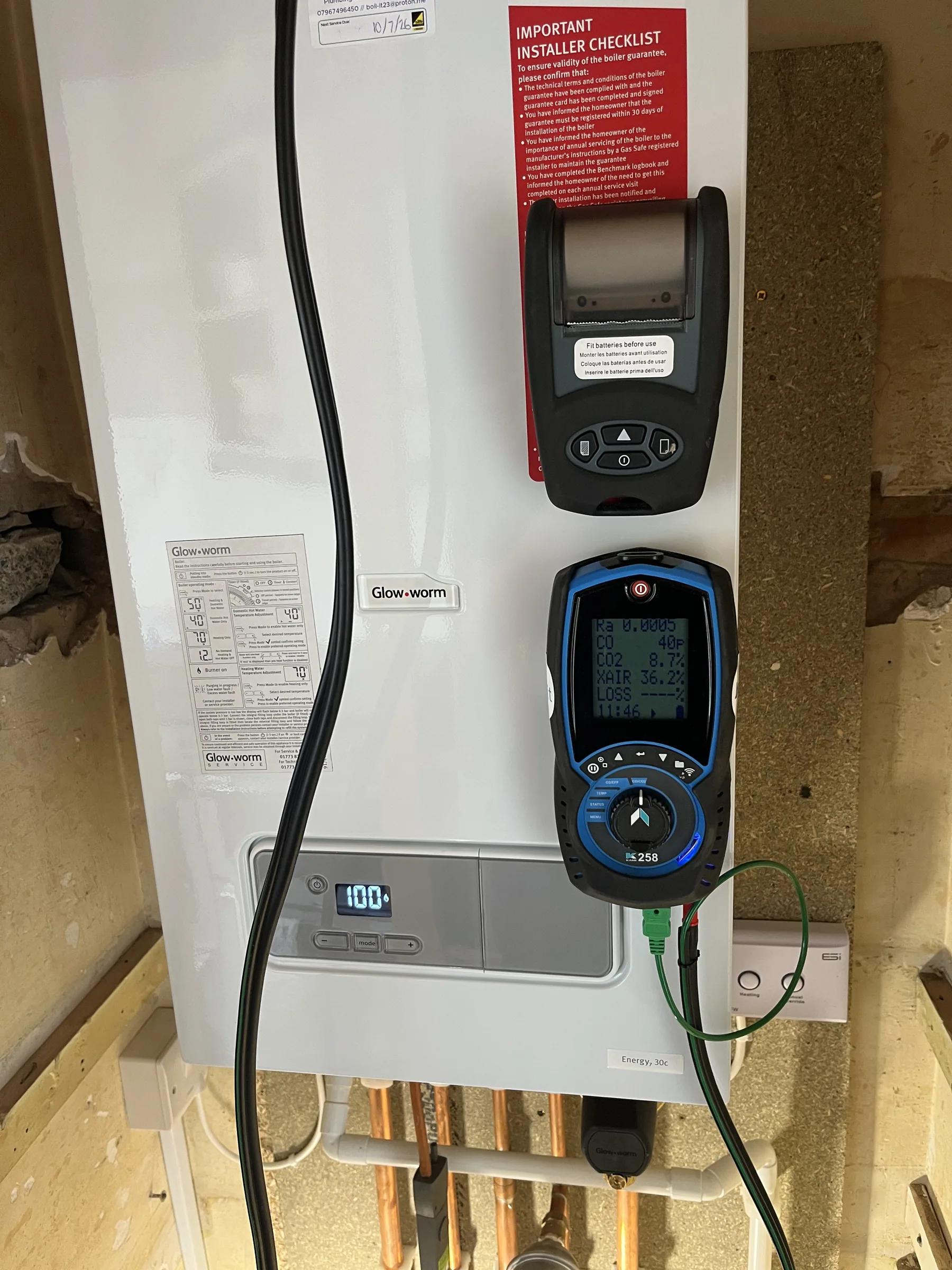 A combustion analyser connected to a wall-mounted boiler beside the gas meter