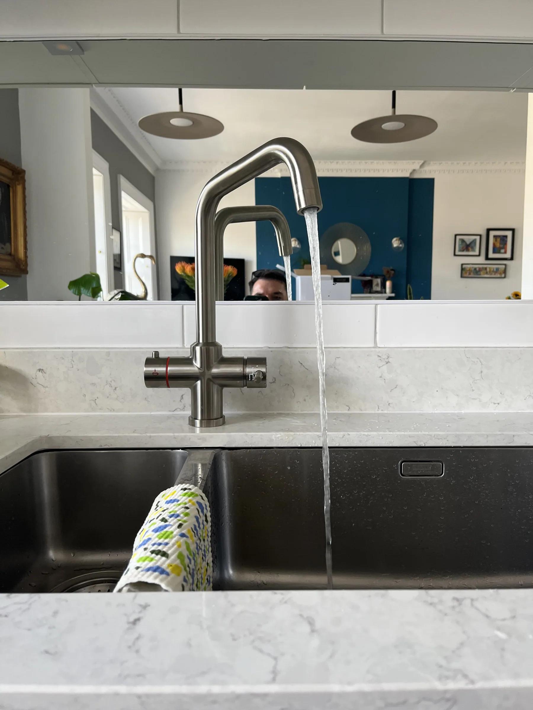 A newly fitted kitchen mixer tap running into a stainless steel sink