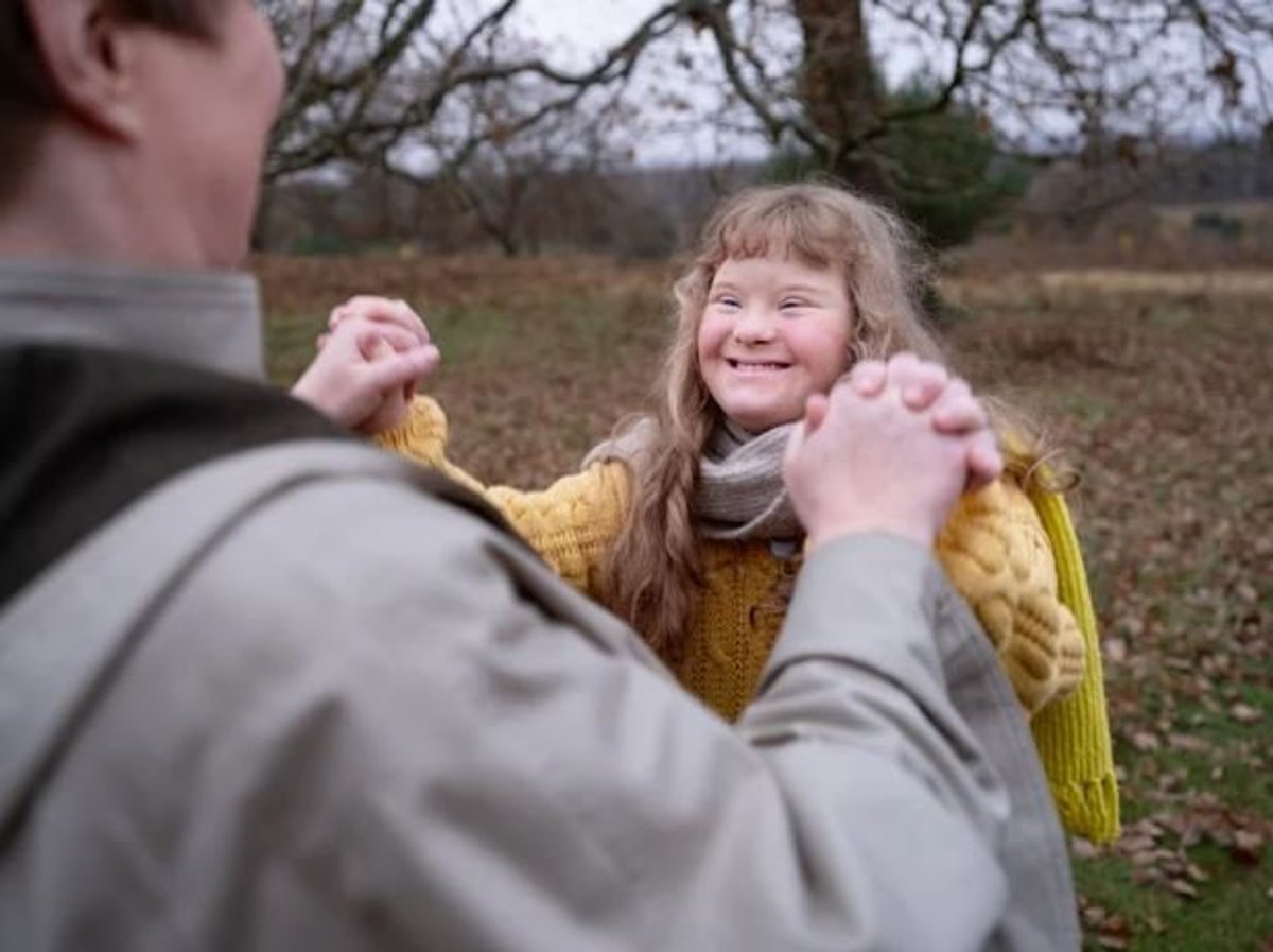 Smiling girl with Down syndrome playing outdoors with an adult in autumn