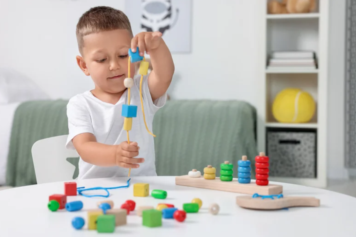 Young boy threading wooden beads onto a string to practise fine motor control