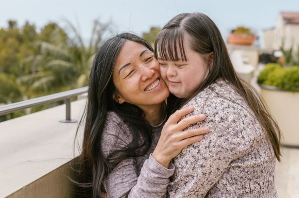 Mother hugging her daughter with Down syndrome on a sunny balcony