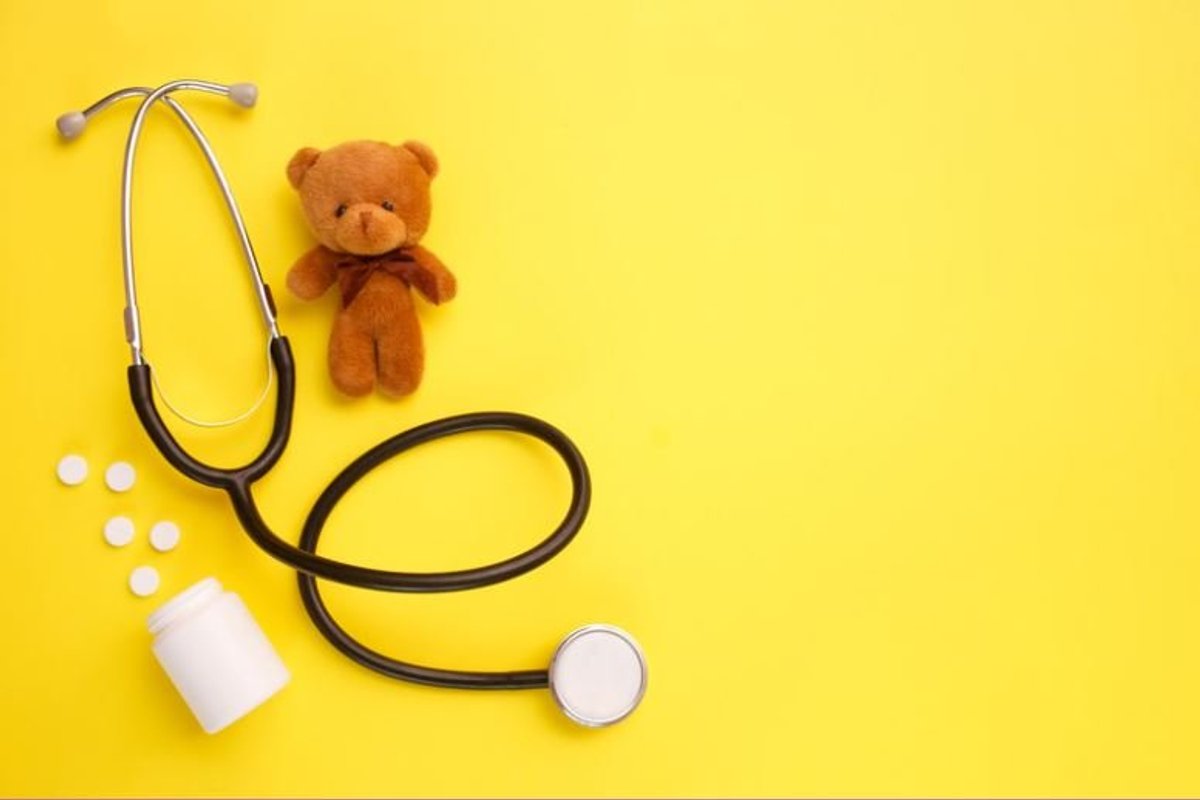 Stethoscope, teddy bear and supplement tablets on a yellow background