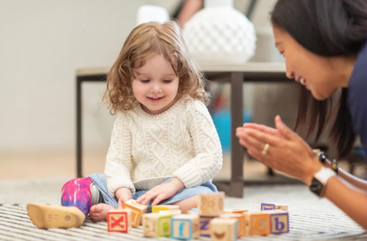 Toddler stacking wooden letter blocks while an adult claps encouragement