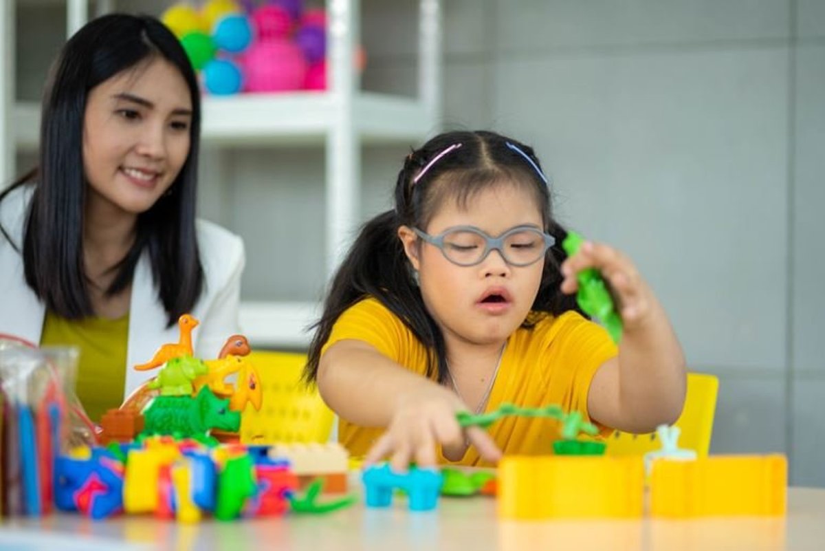 Girl with glasses playing with colourful blocks while a therapist watches