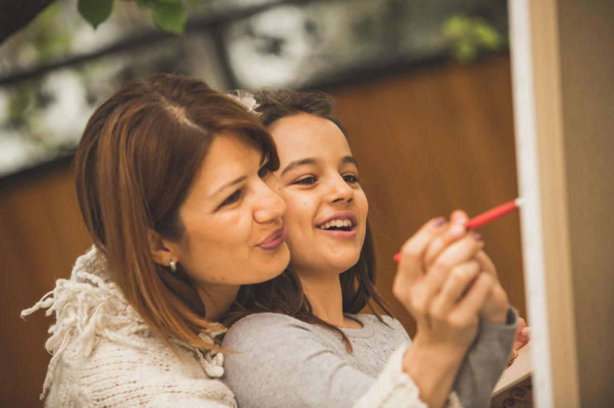 Mother encouraging her daughter as she draws on a whiteboard