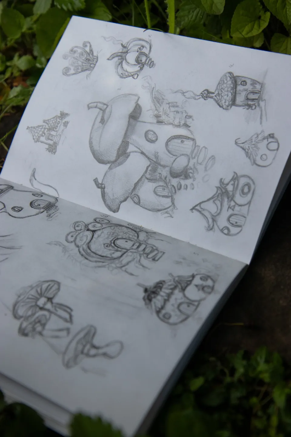 A sketchbook spread filled with drawings of fairy houses in mushrooms, ferns, flowers and acorns.