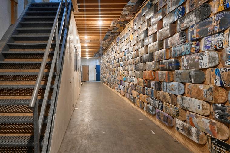 De gang langs een muur die helemaal bedekt is met oude skateboards.
