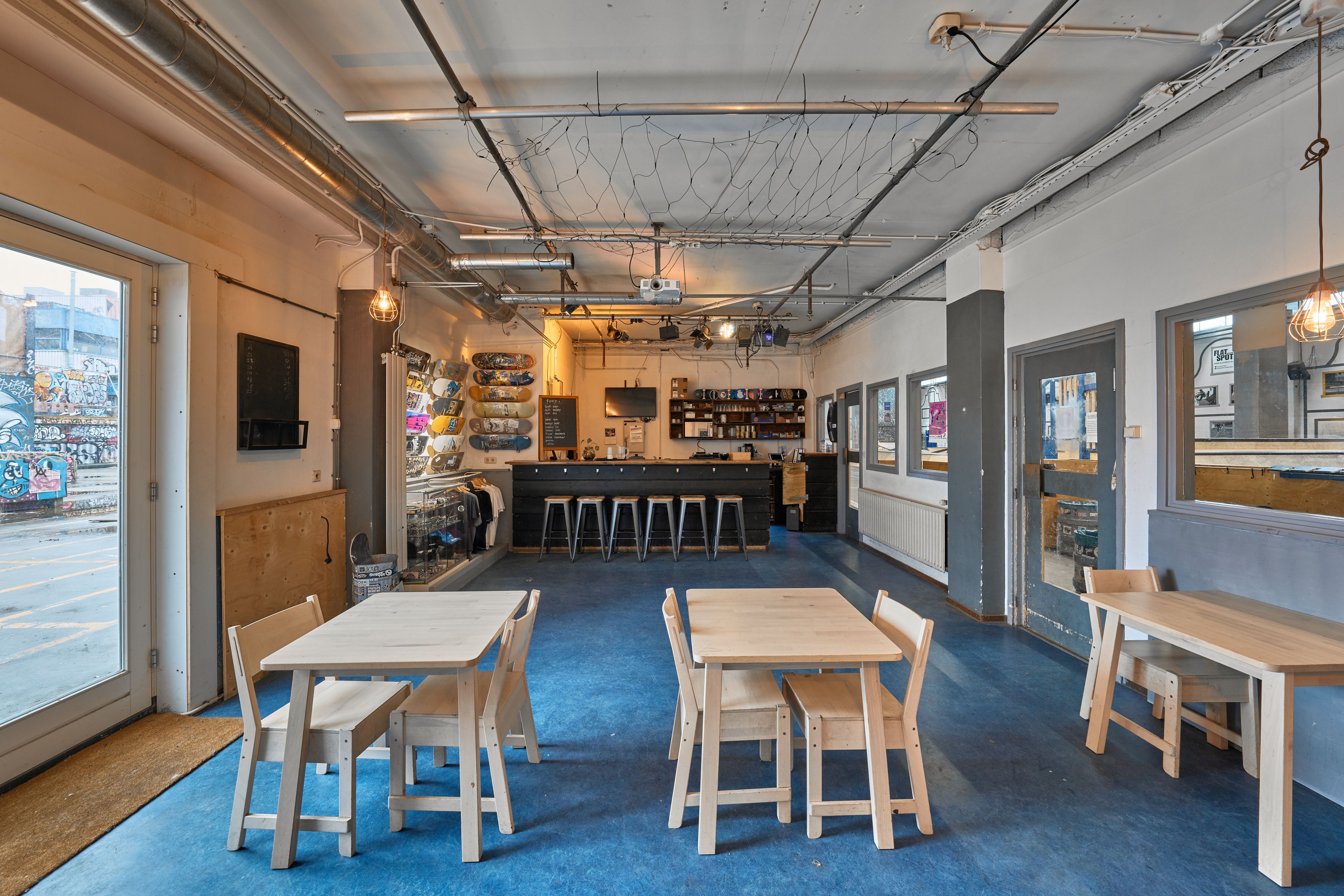 [PLACEHOLDER] Skatecafe 030 met de bar achterin en houten tafels op de blauwe vloer