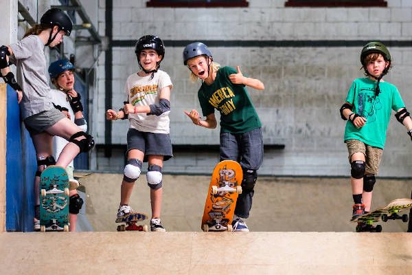 Vier kinderen met hun boards, lachend, met de duimen omhoog.
