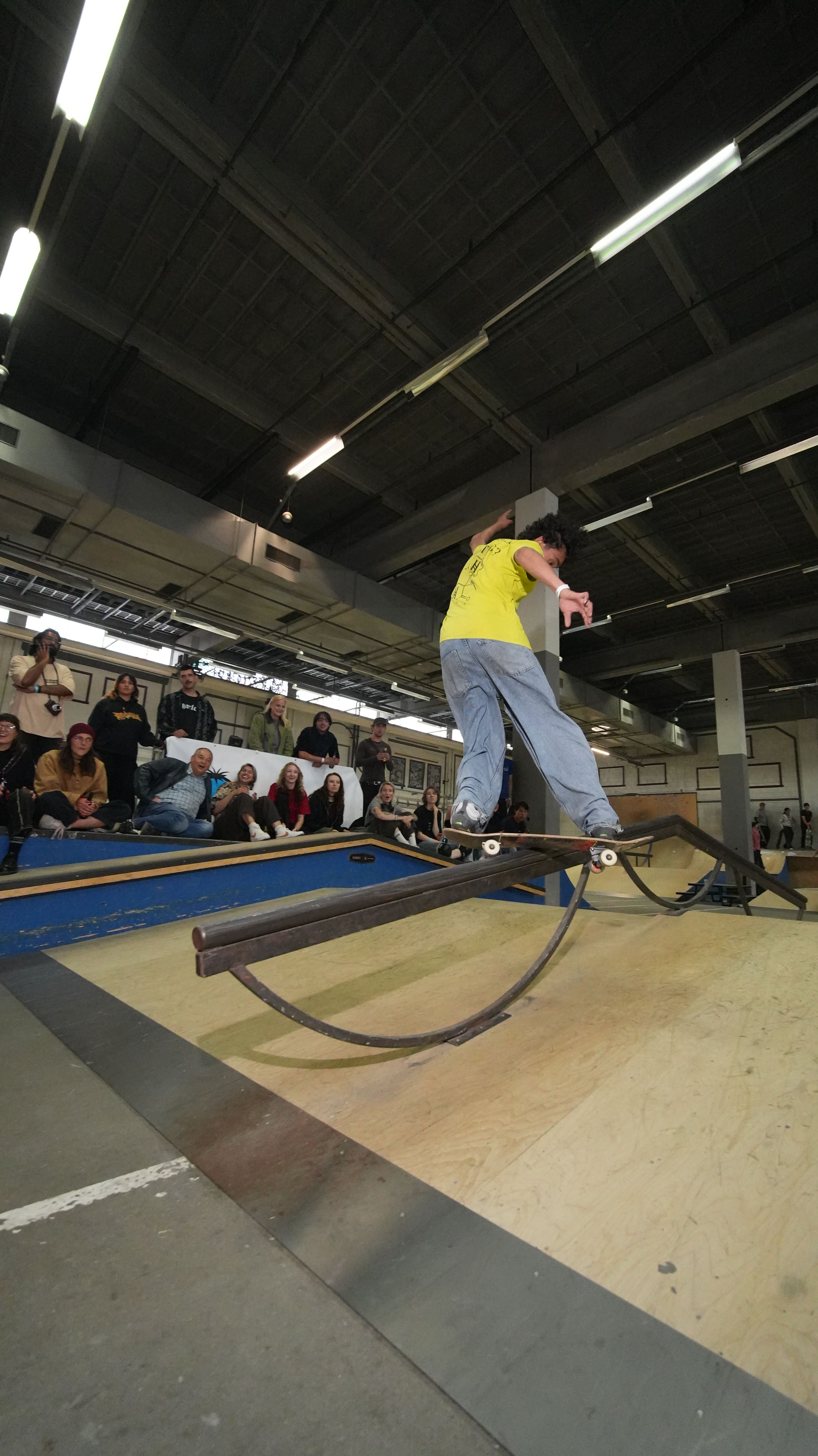 [PLACEHOLDER] Een skater landt op de gebogen rail terwijl iedereen toekijkt