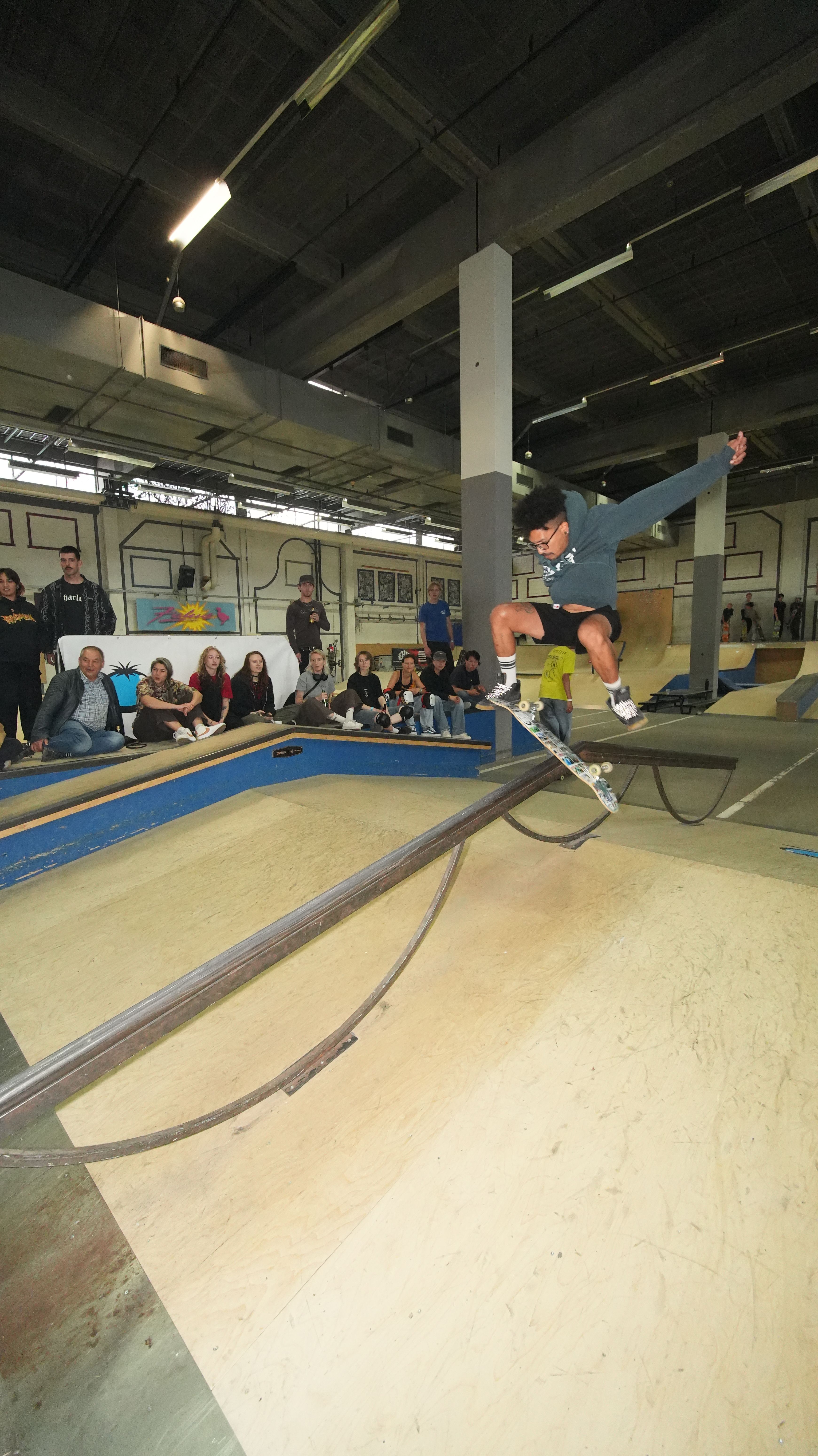 [PLACEHOLDER] Een skater vliegt over de gebogen rail, publiek langs de kant