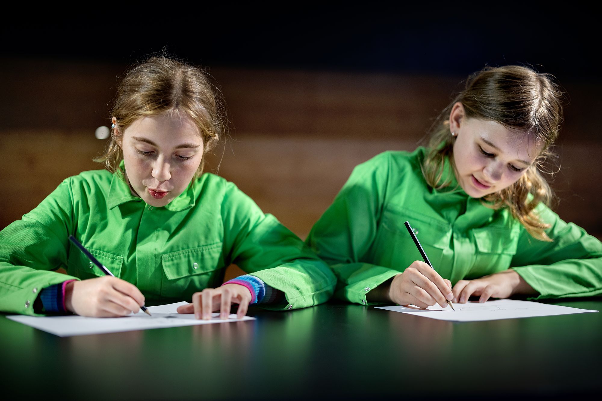 Twee meisjes in groene pakken tekenen op een blaadje.