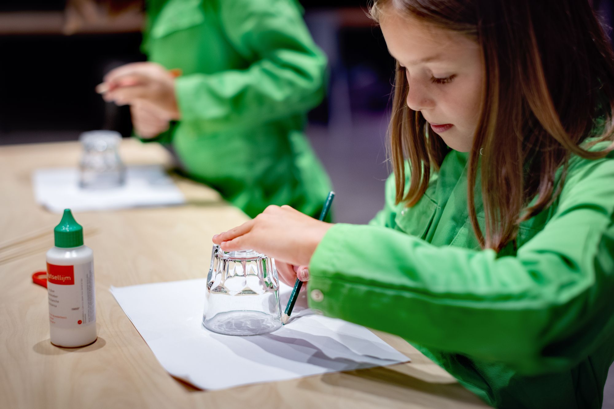 Een meisje trekt een cirkel op papier om een glas