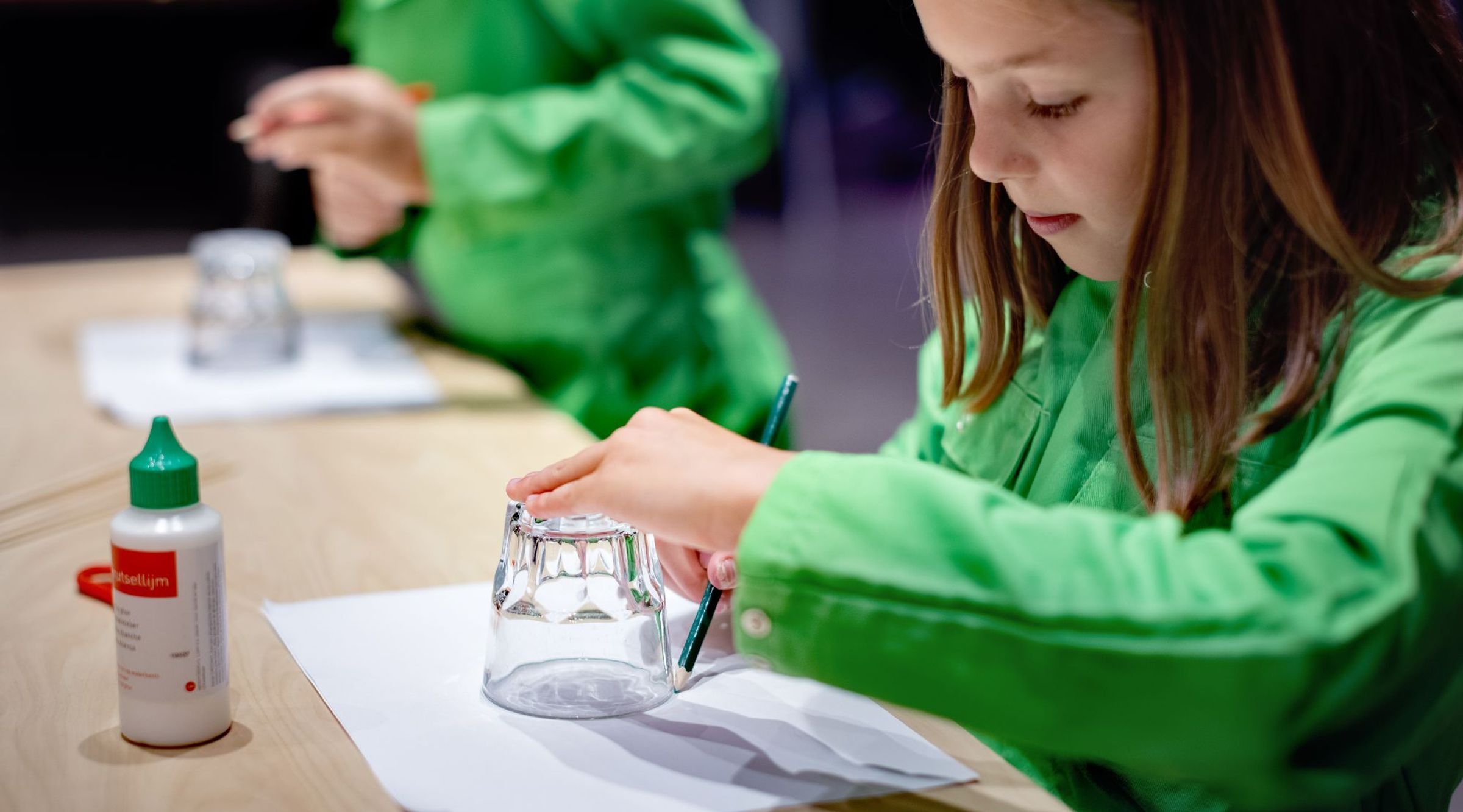 Een meisje trekt een cirkel op papier om een glas