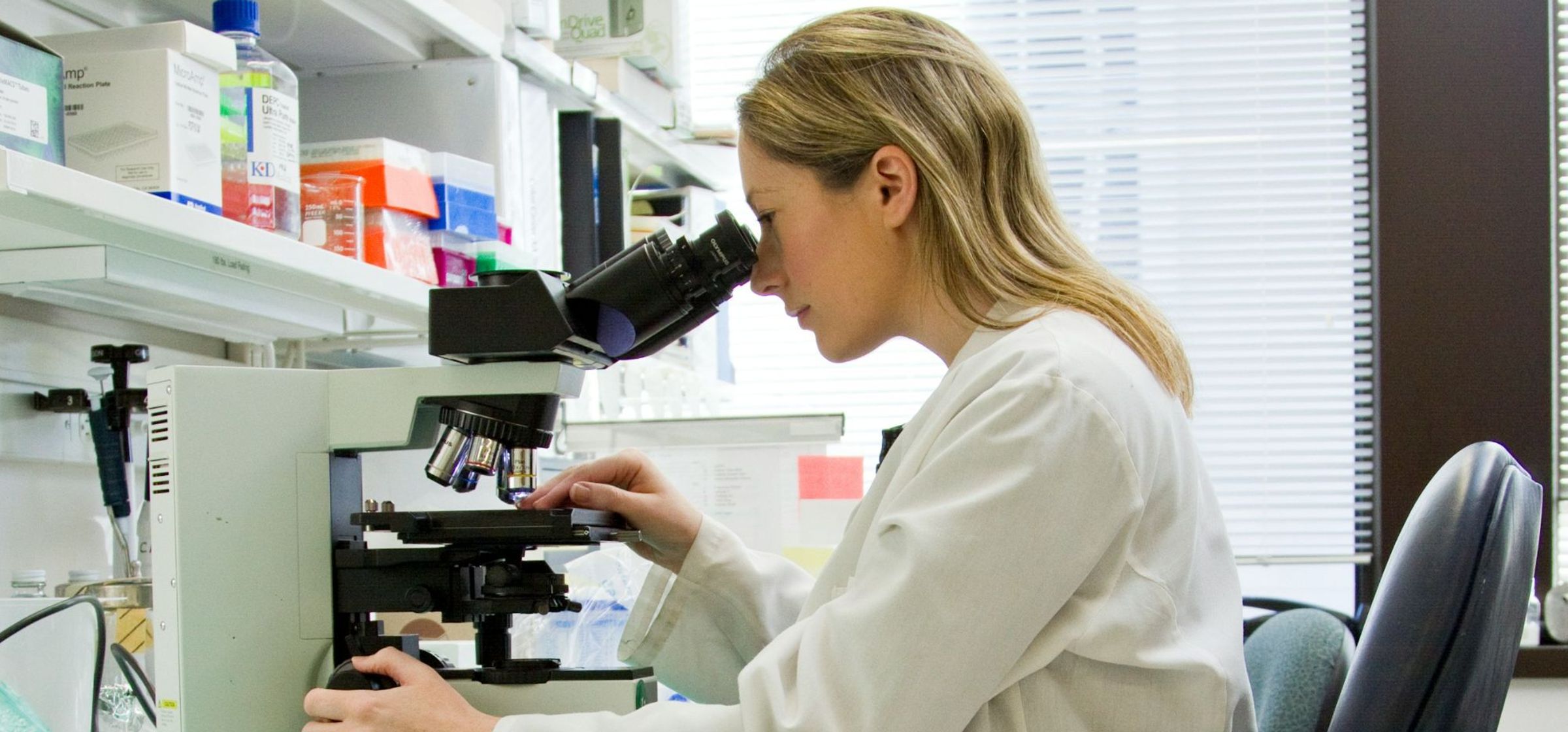 Een vrouw zit achter een microscoop.