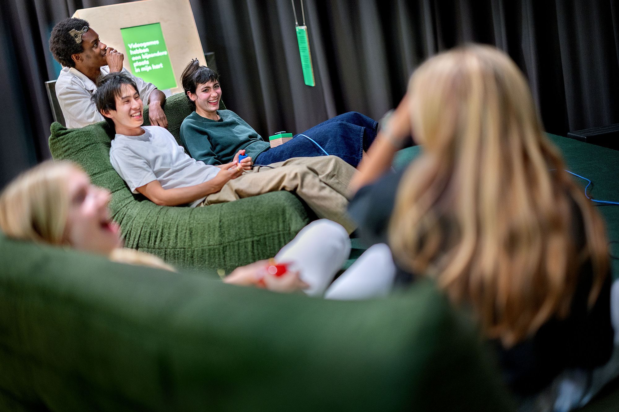 Young people are hanging around on couches with game controllers in their hands.
