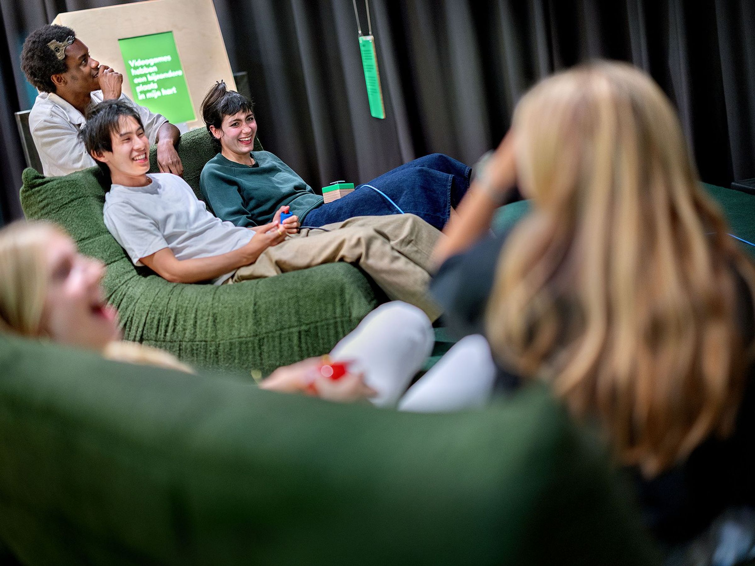 Jongeren zitten op banken met gameconsoles in hun hand en lachen