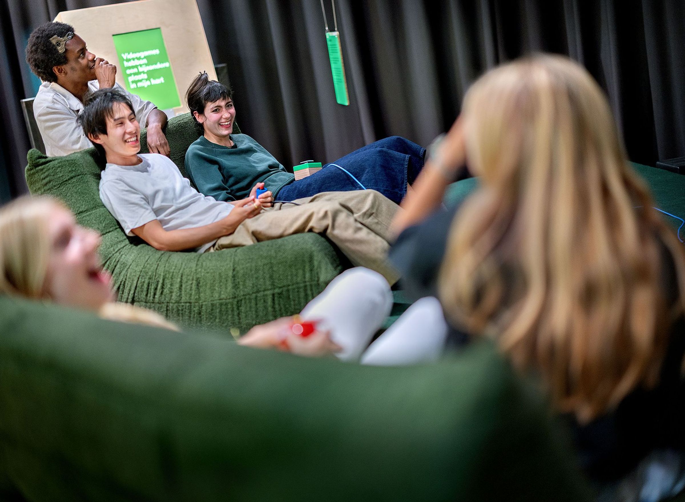 Young people are hanging around on couches with game controllers in their hands.