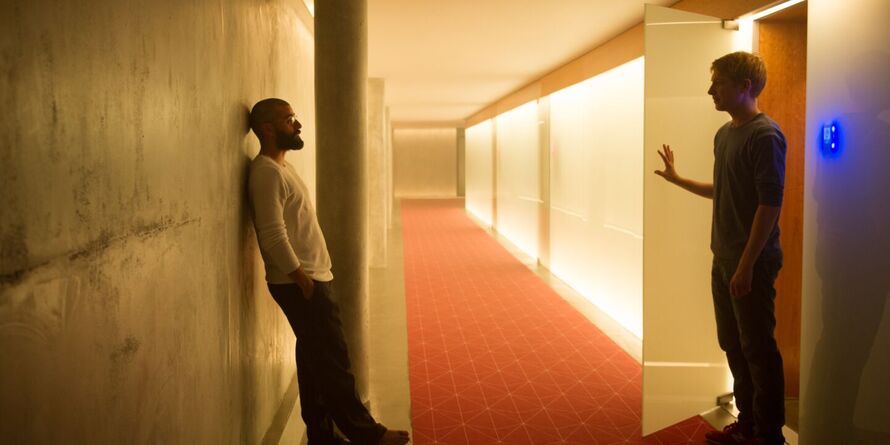Two men are standing facing each other in a corridor.