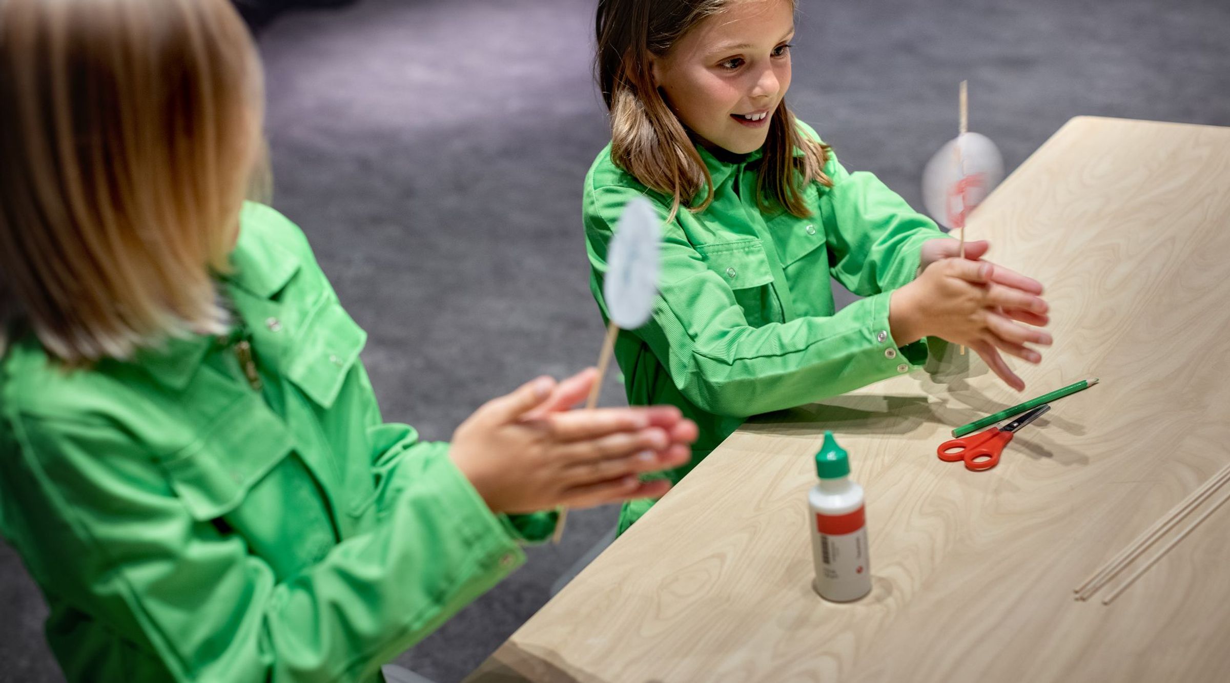 Twee meisjes draaien satéprikkers waaraan rondjes papier geplakt zijn