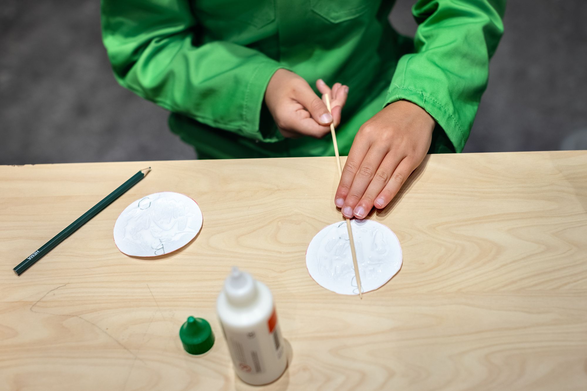 Er wordt een satéprikker aan een rondje papier gelijmd