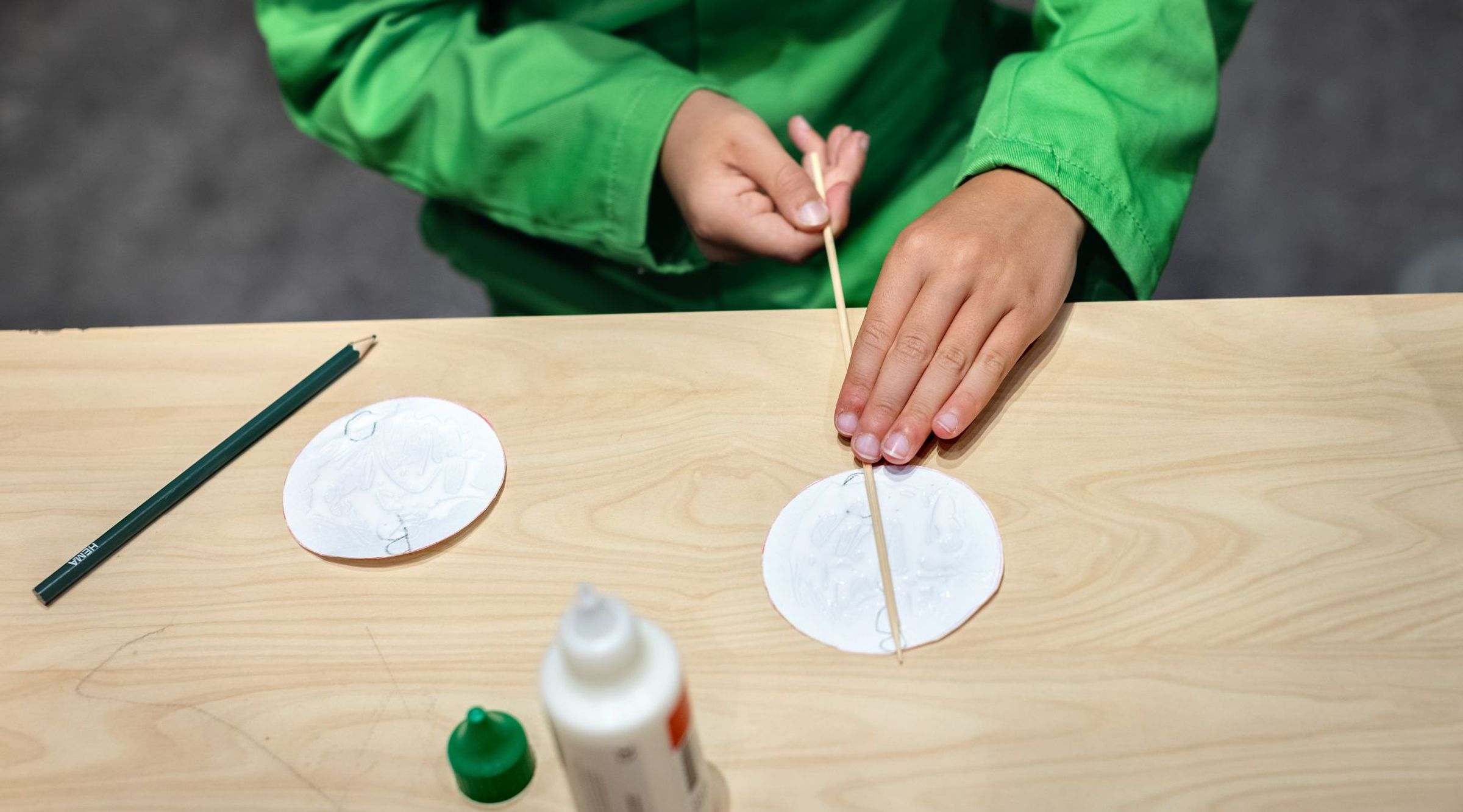 Er wordt een satéprikker aan een rondje papier gelijmd