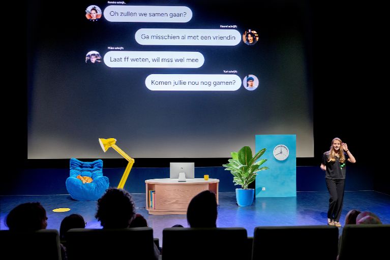 een vrouw staat voor een groot beeldscherm met daarop een een chatgesprek