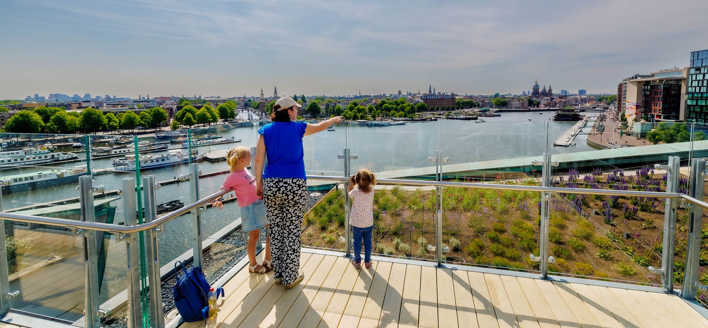 A woman with two kids standing on a viewpoint facing the skyline of Amsterdam
