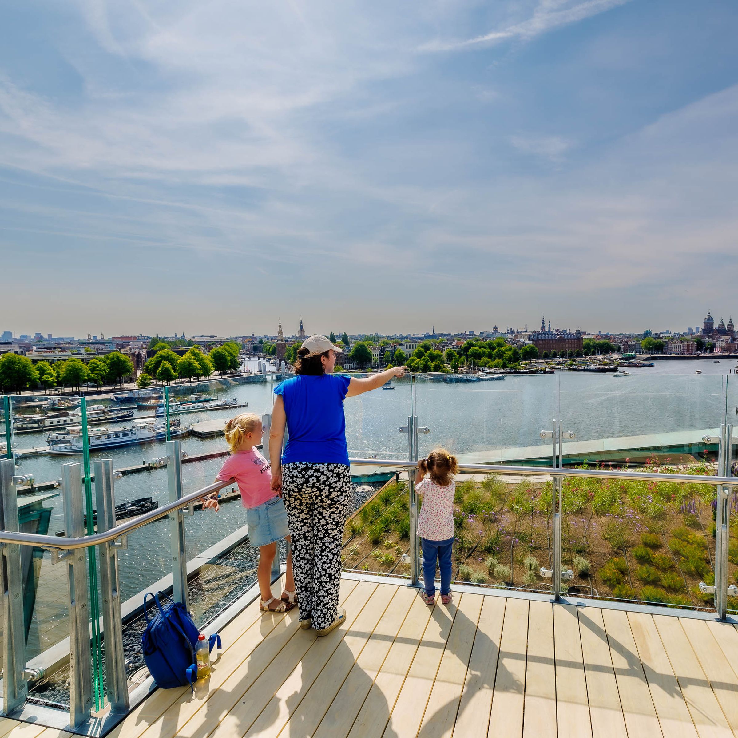 A woman with two kids standing on a viewpoint facing the skyline of Amsterdam