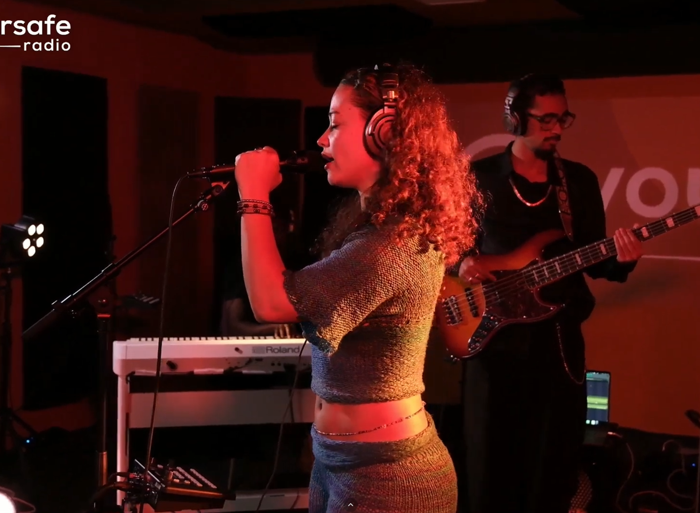 Een vrouw met krullen zingt in een microfoon met een koptelefoon op.
