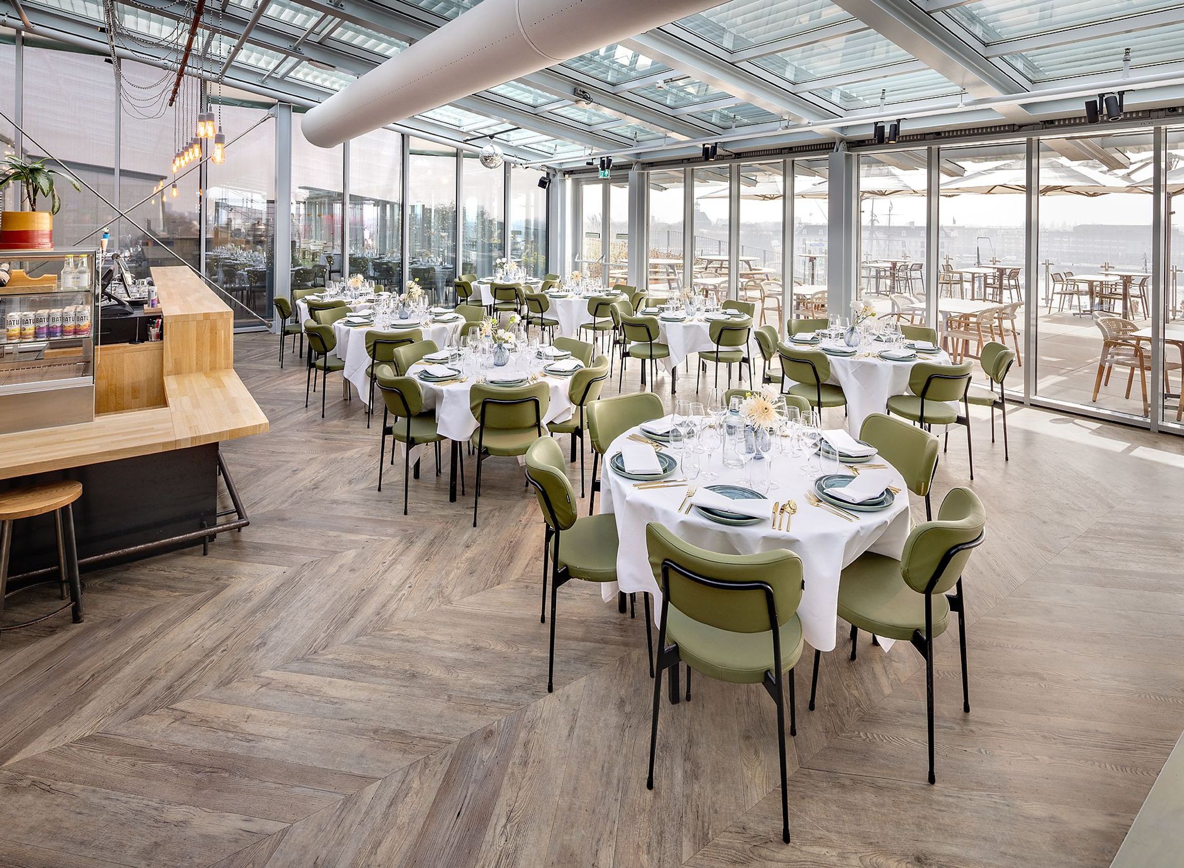 Een grote zaal met ronde witte tafels en groene stoelen