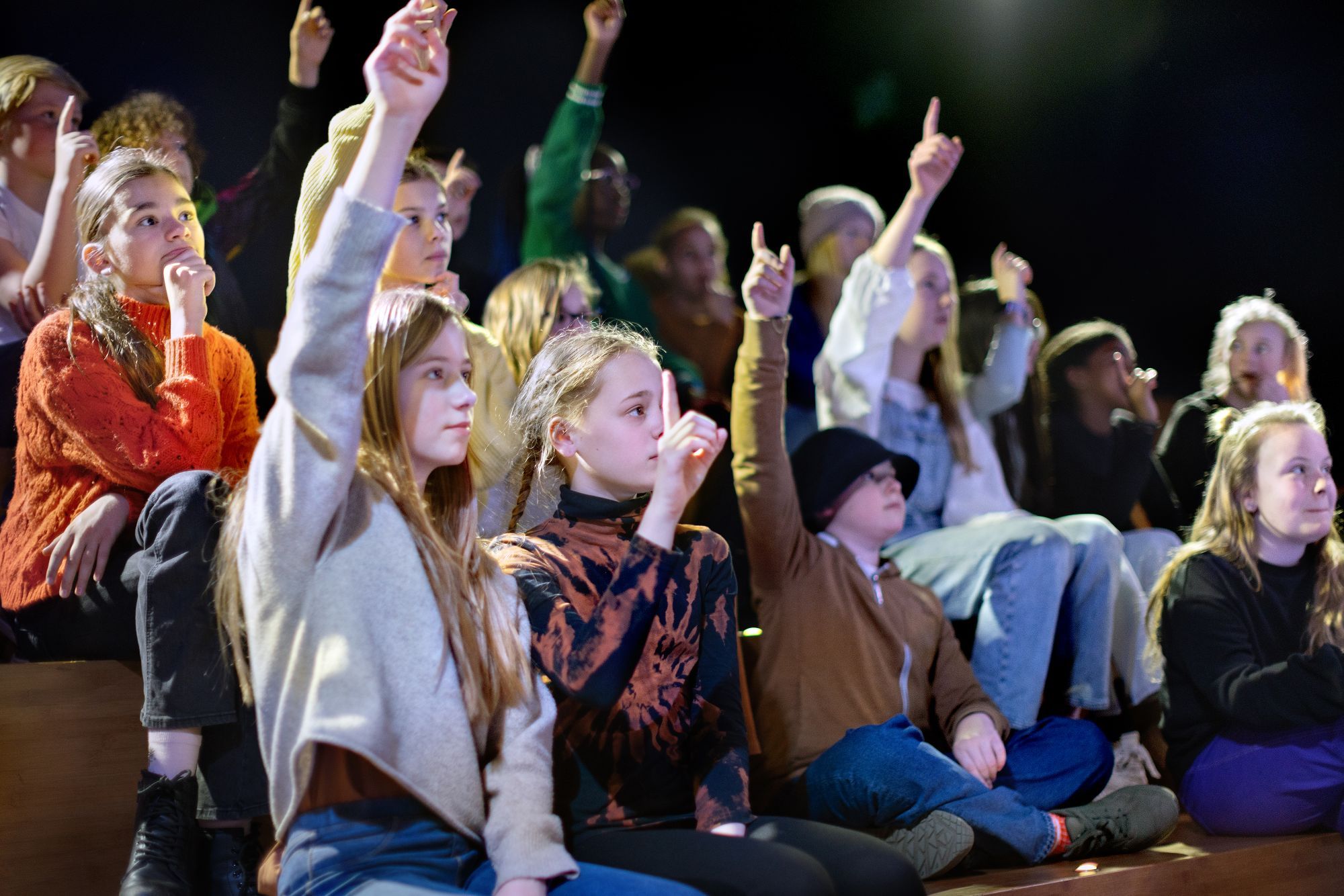 children in an audience raise their hands to answer a question