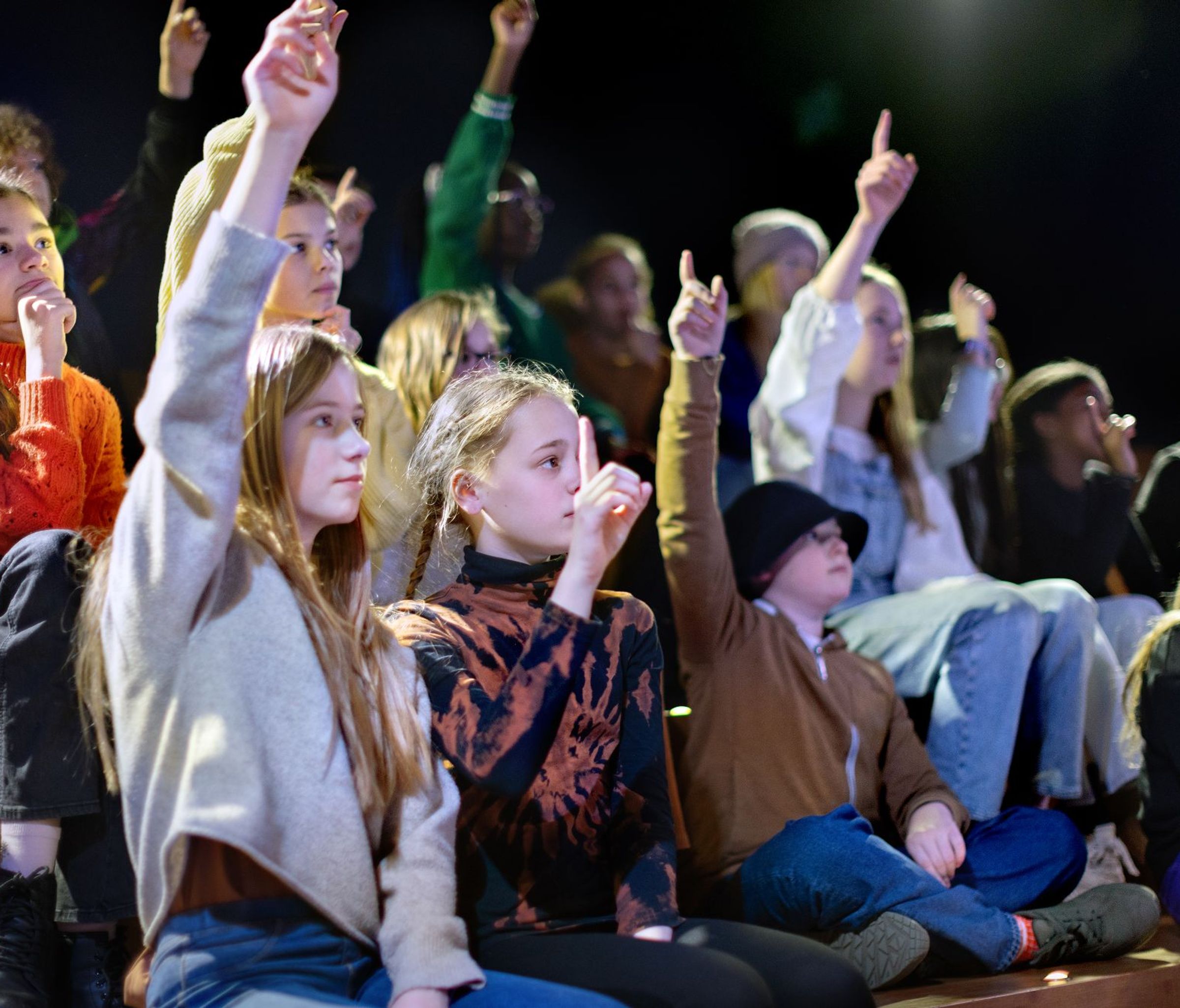children in an audience raise their hands to answer a question