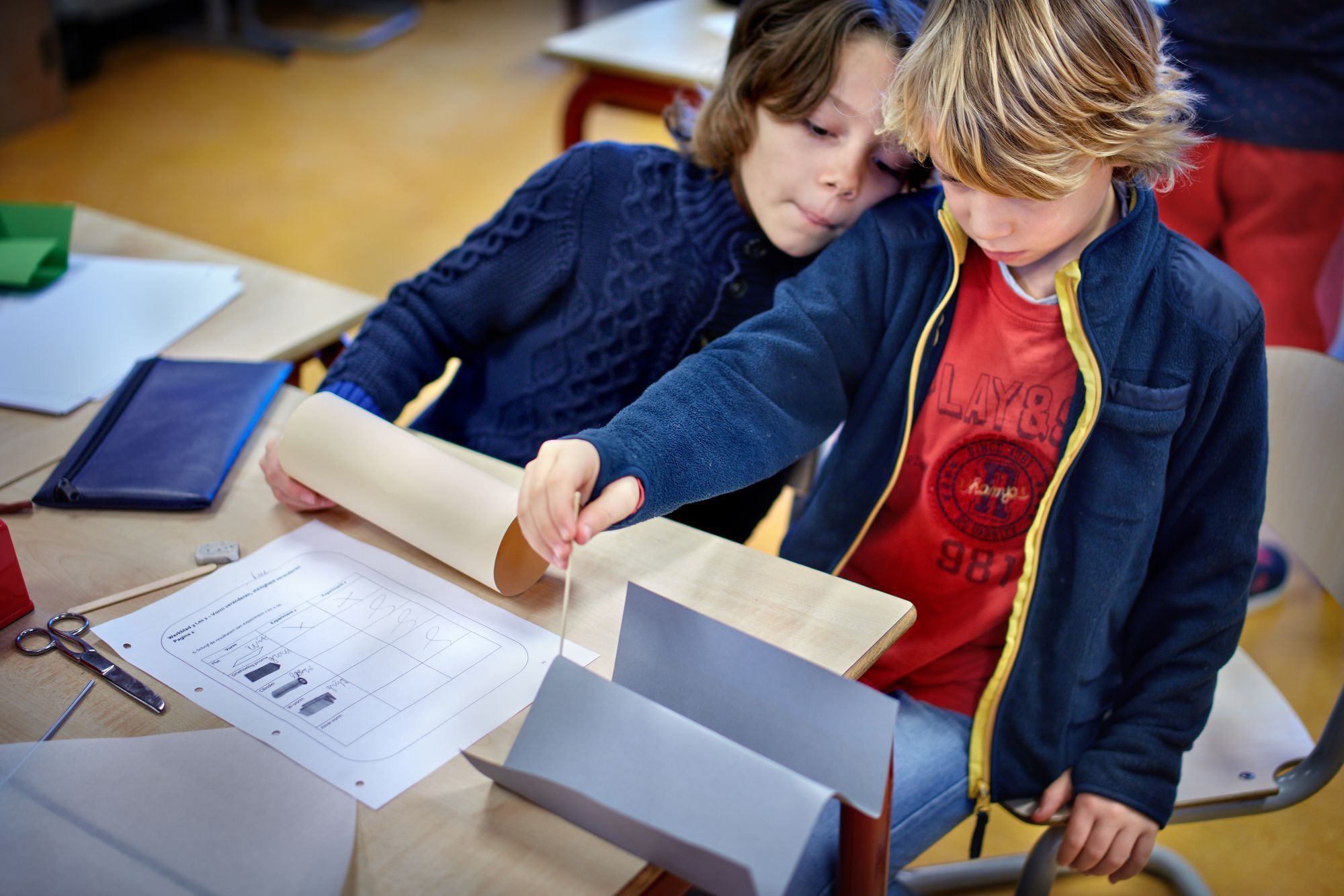 Twee jongens zijn bezig met vellen papier en satéprikkers.