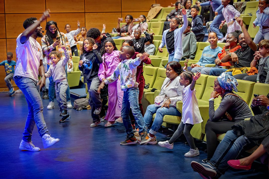 een man doet een dans voor aan een zaal kinderen die meedansen