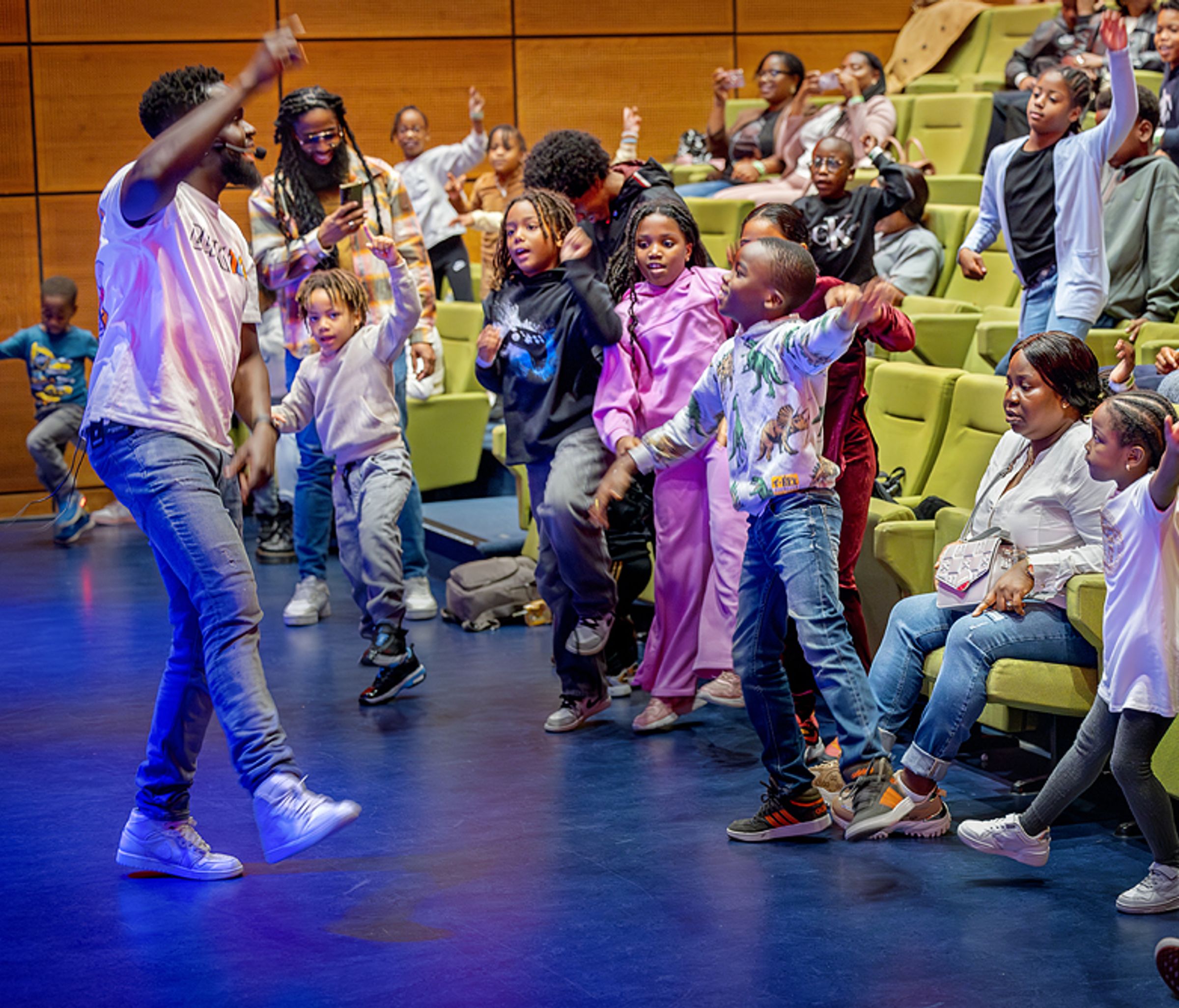 een man doet een dans voor aan een zaal kinderen die meedansen