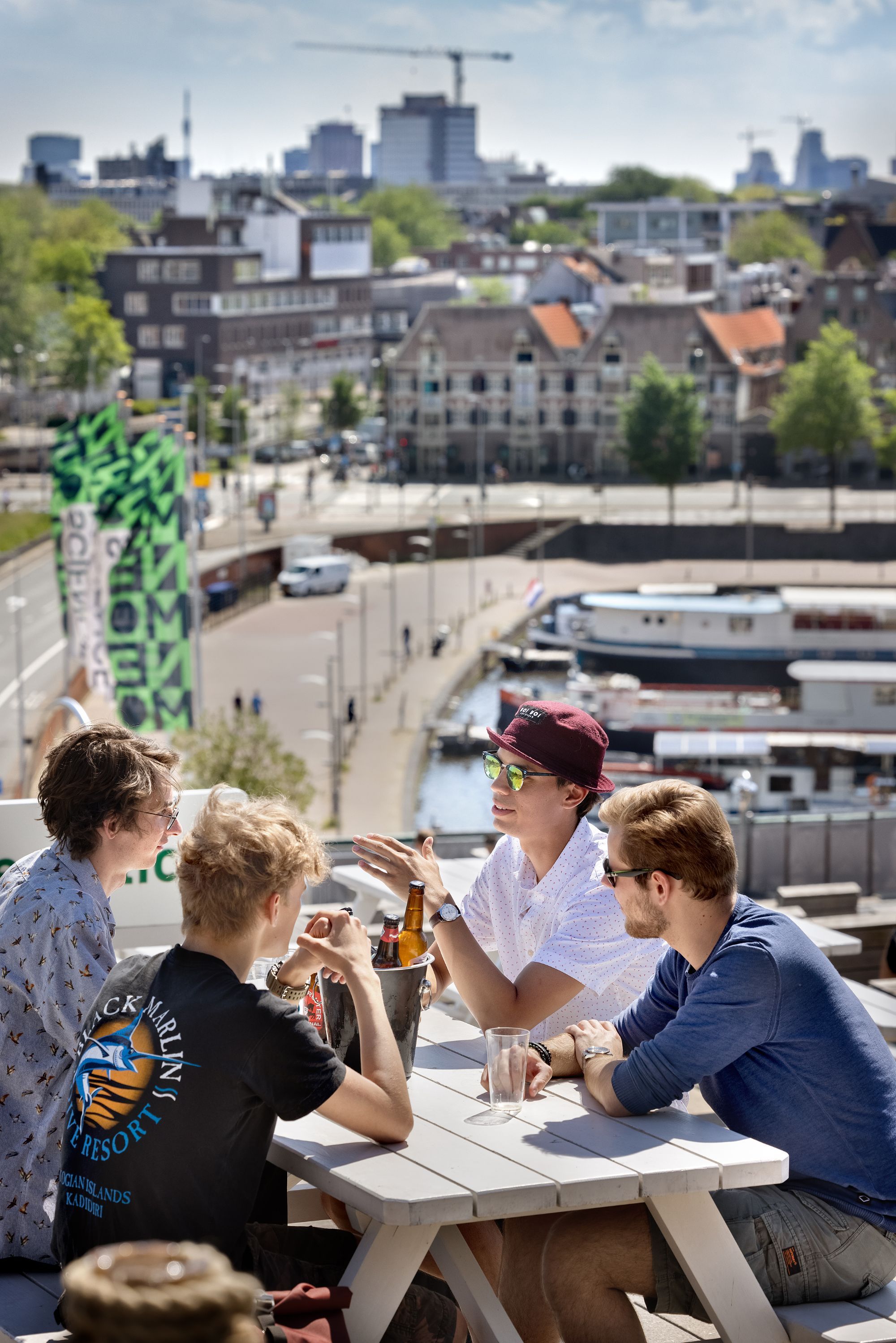 Vier mannen zitten om een witte tafel heen met een emmer drankjes tussen hen in.
