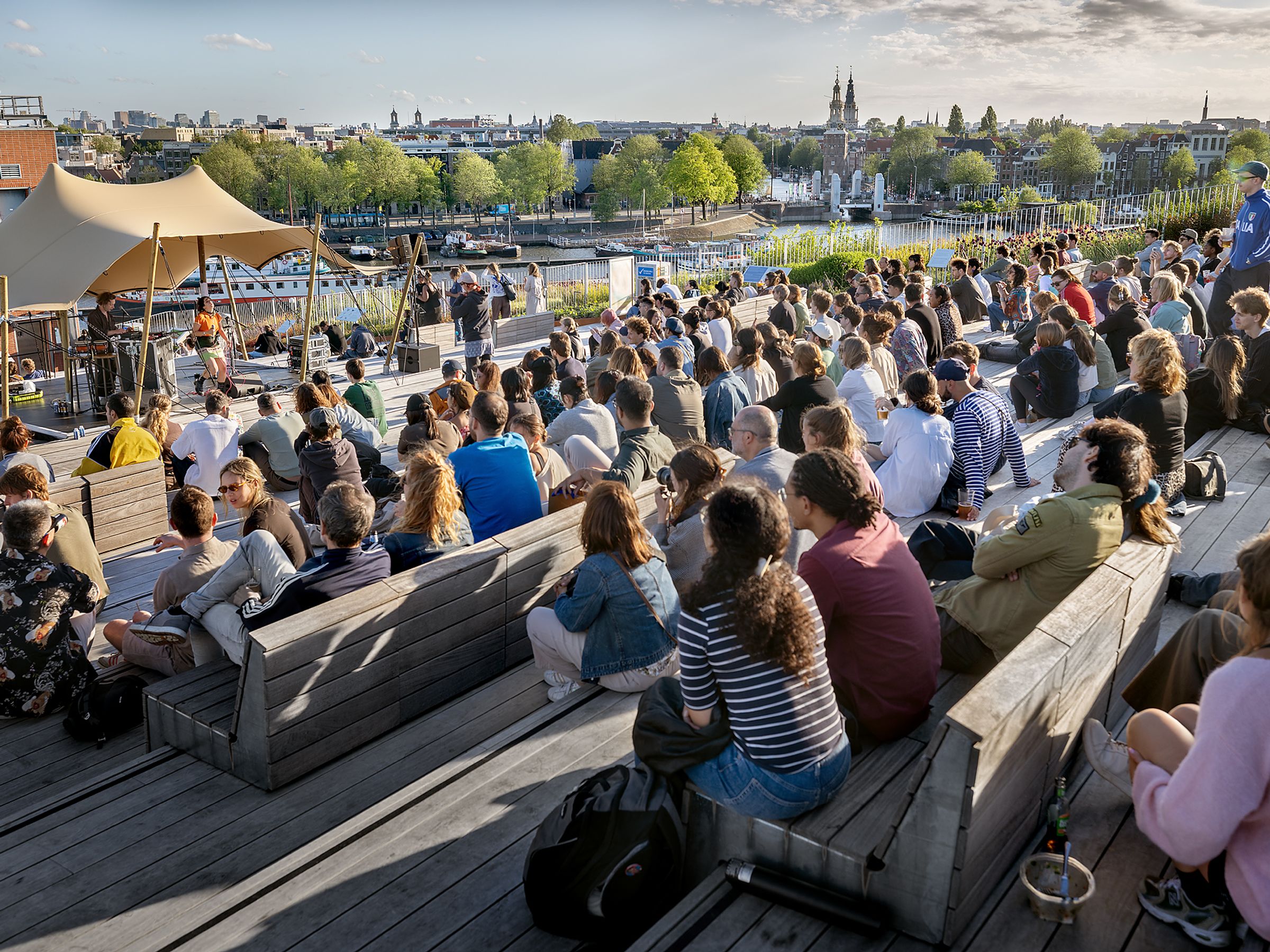 Mensen zitten op houten trappen te luisteren naar live muziek in de buitenlucht.