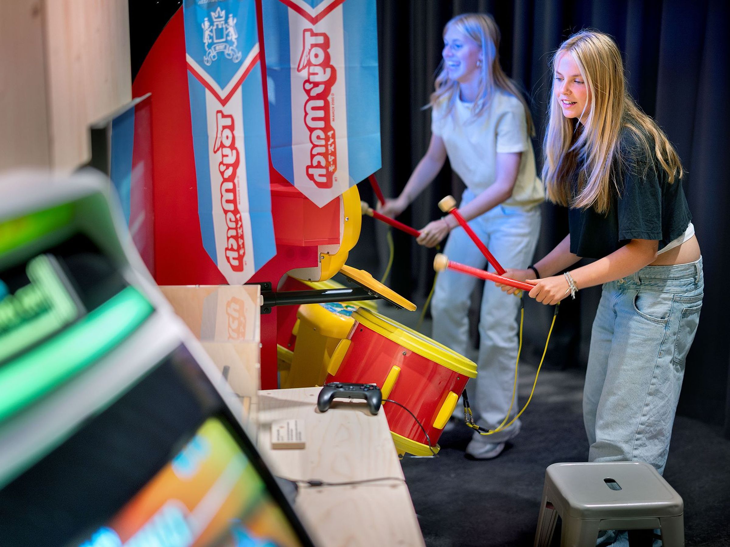 Twee meisjes staan bij een arcadegame waar ze moeten slaan op trommels met stokken