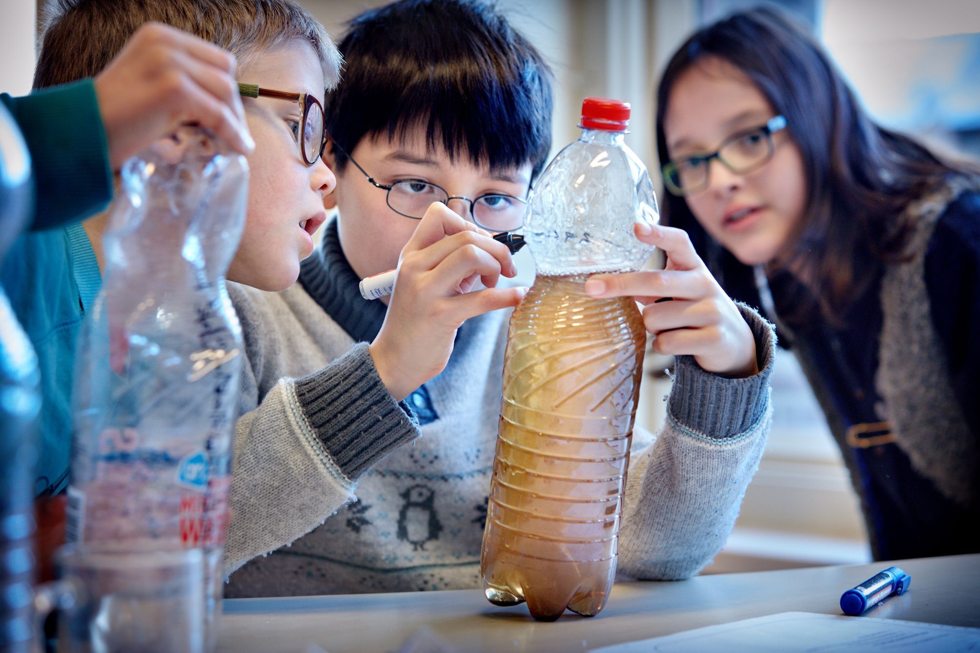 Een jongen zet een streep op een fles waarin vies water zit.