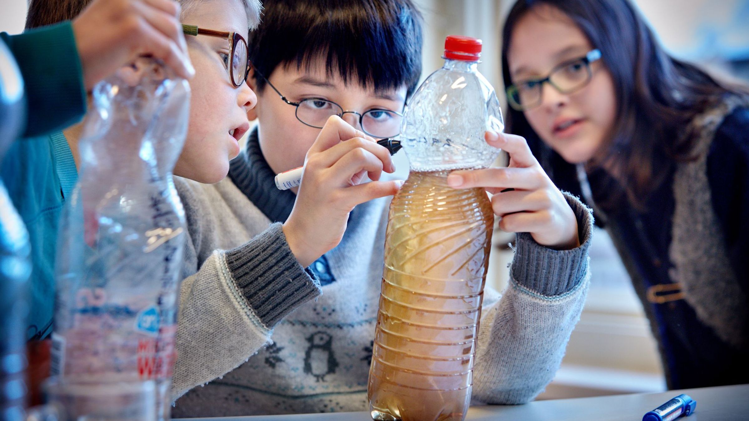 Een jongen zet een streep op een fles waarin vies water zit.
