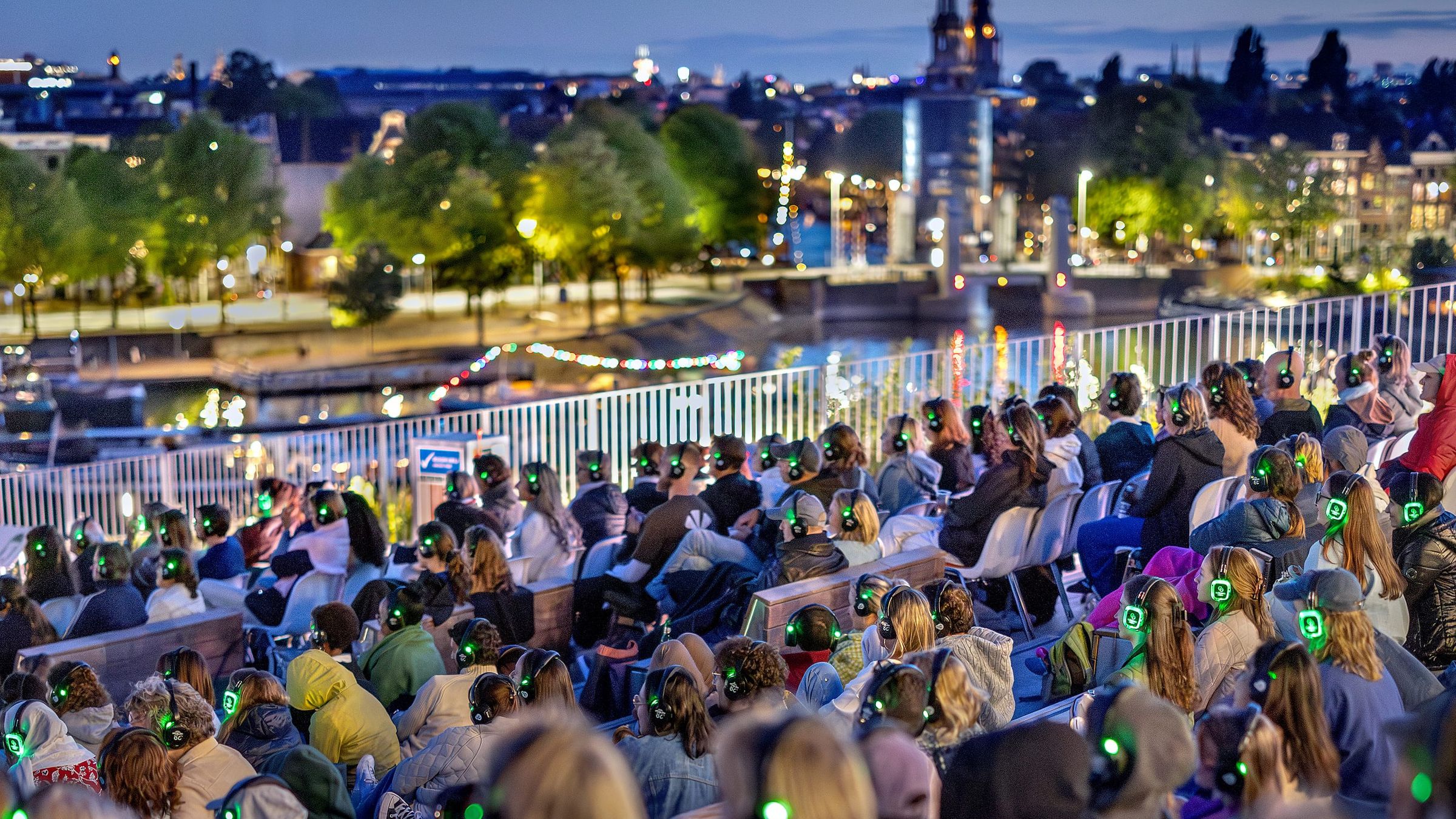Publiek met koptelefoons op het dak van NEMO en de skyline van Amsterdam op de achtergrond.