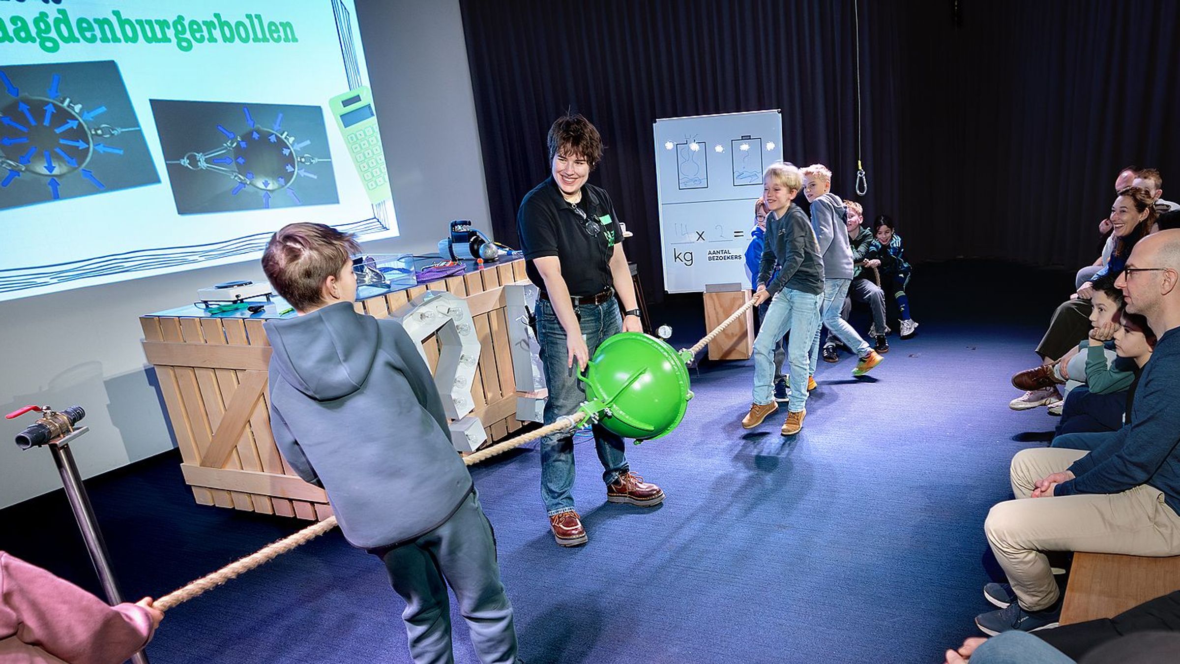 Kinderen proberen een groene bol uit elkaar te halen door aan een touw te trekken, een NEMO-medewerker staat in het midden